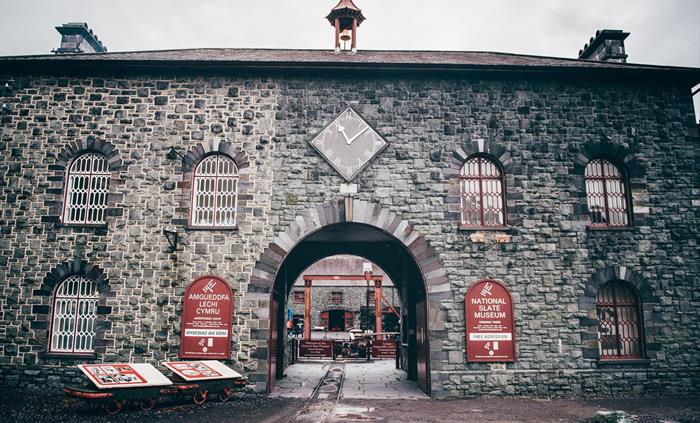 A large stone building, two storeys high, with a large archway in the middle to allow a steam train to enter the yard beyond. .there are arched window